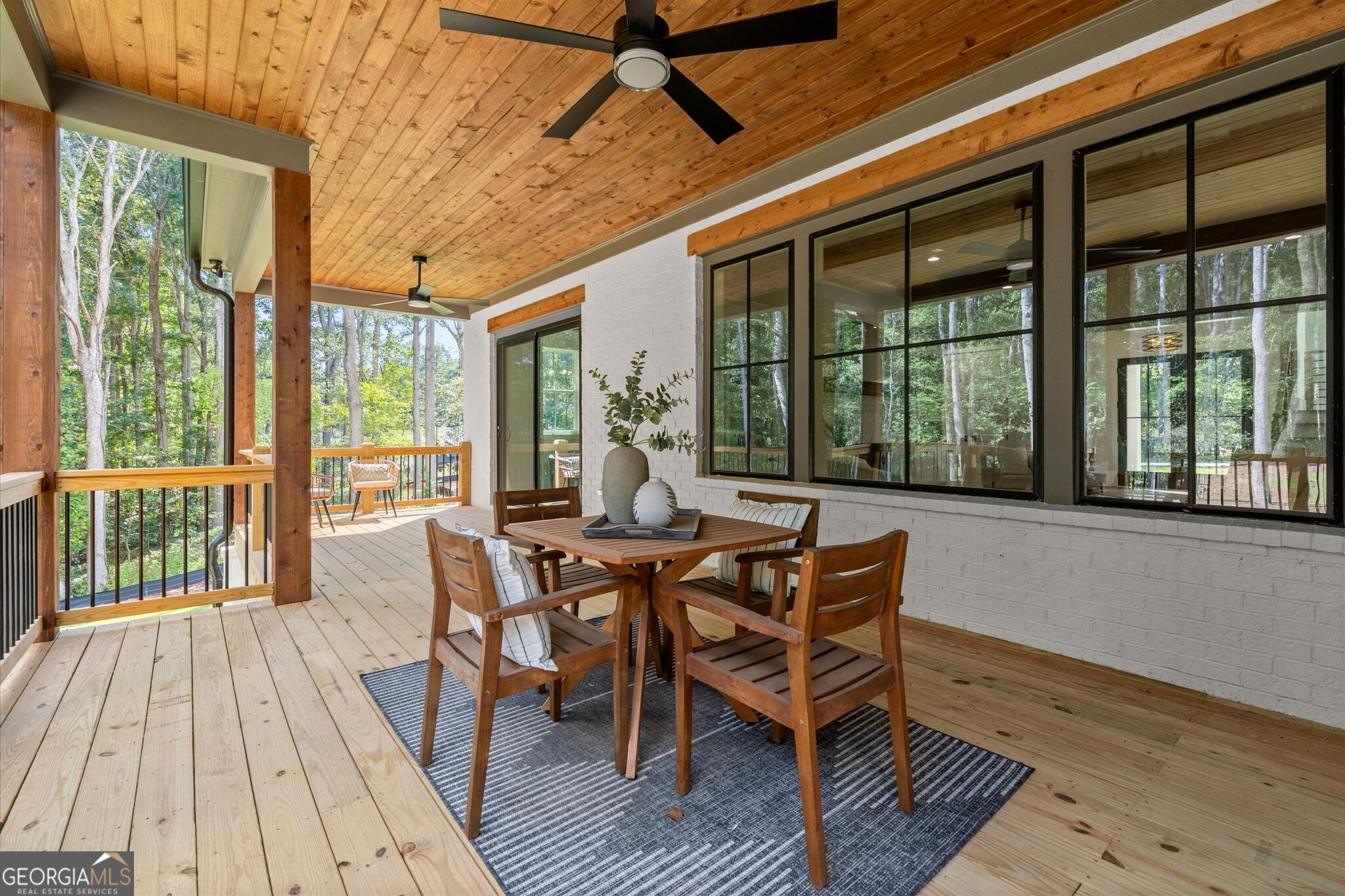 Covered porch with a wood ceiling, dining set, and views of surrounding trees.