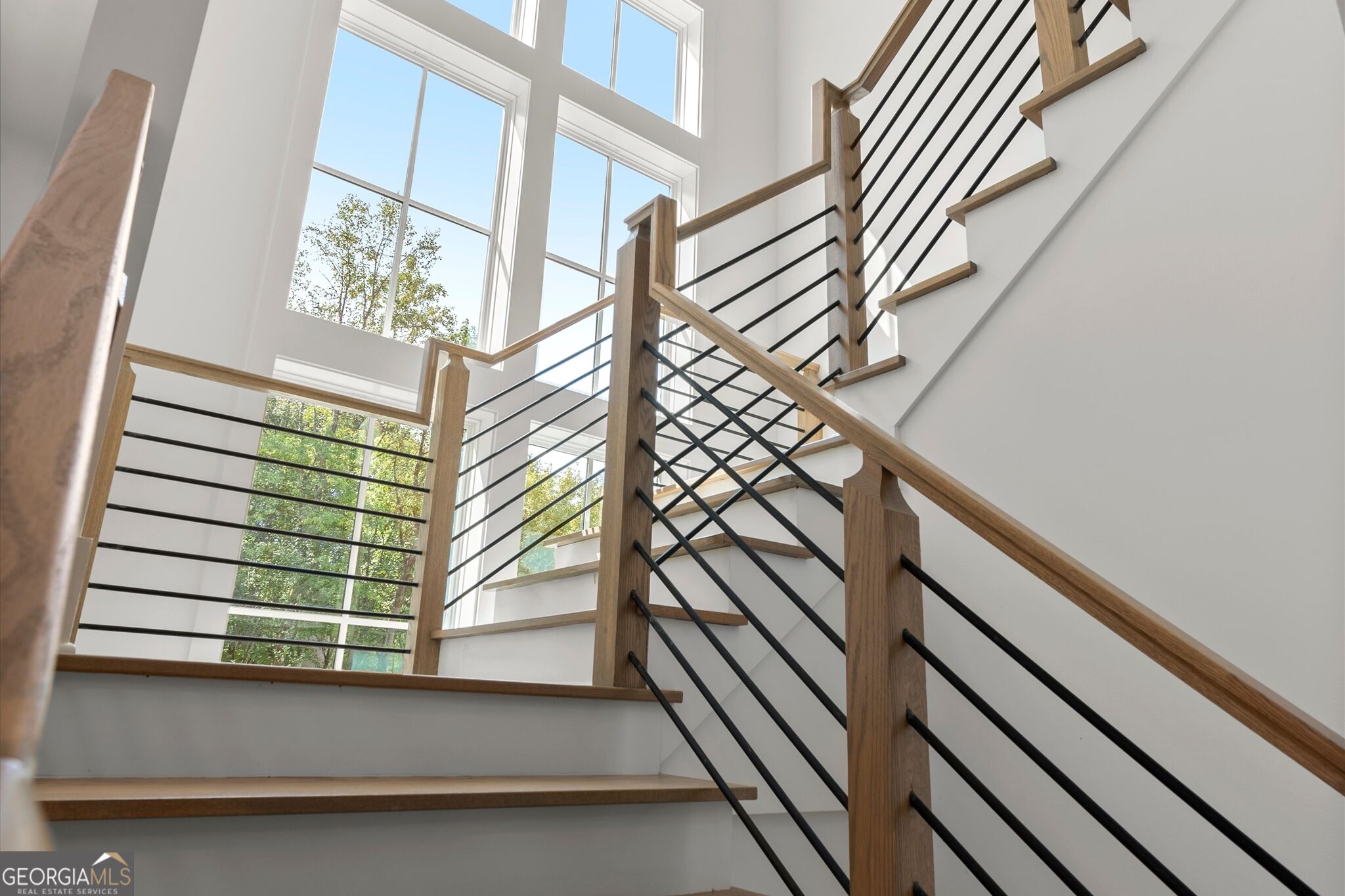 Interior staircase with wood and black metal railings beside tall windows.
