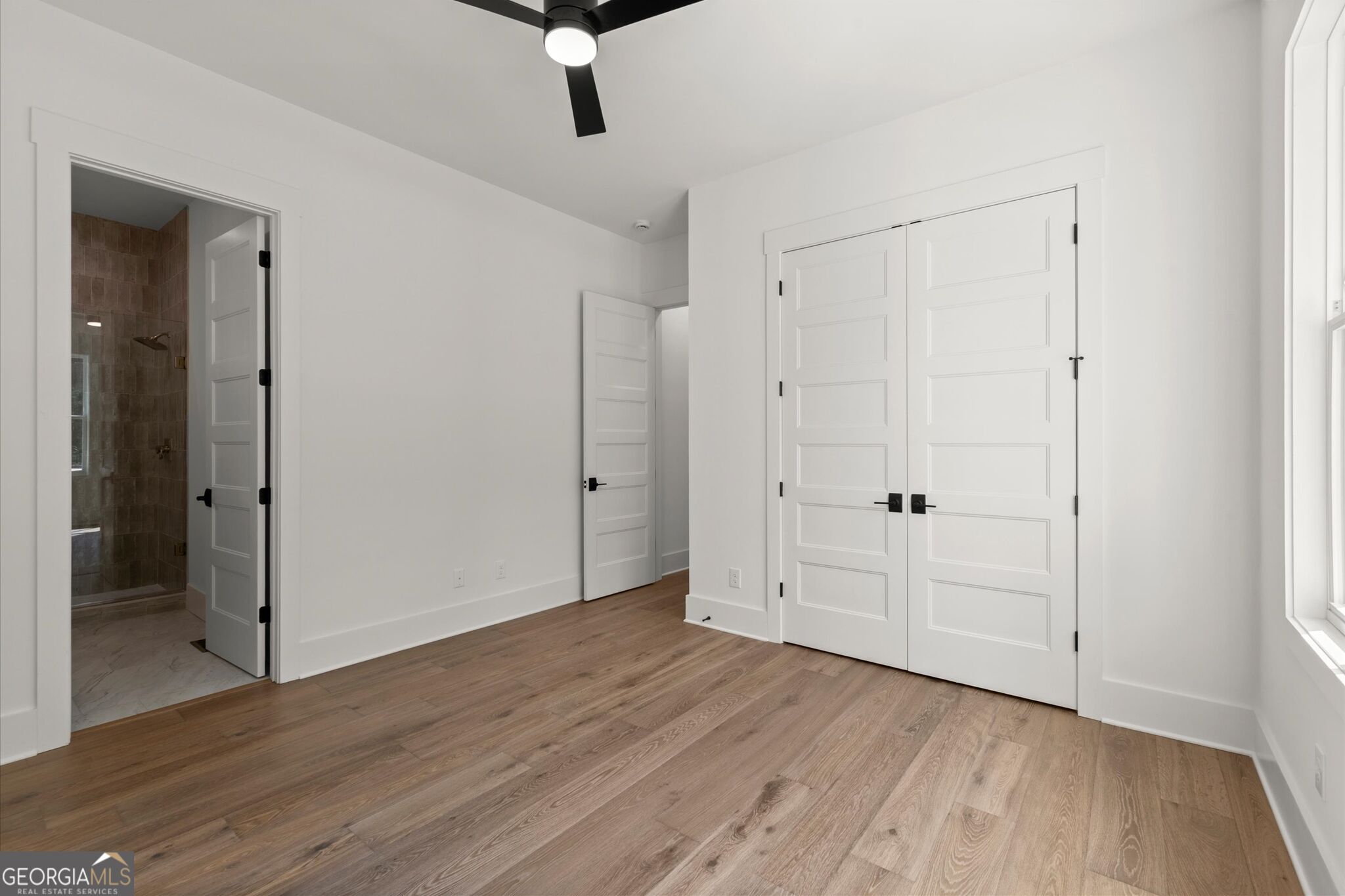 Empty bedroom with wood floors, double closet doors, and an open doorway to a tiled bathroom.