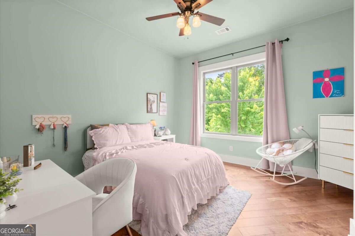Bedroom with a pink bedspread, pale green walls, and a large window overlooking leafy trees.