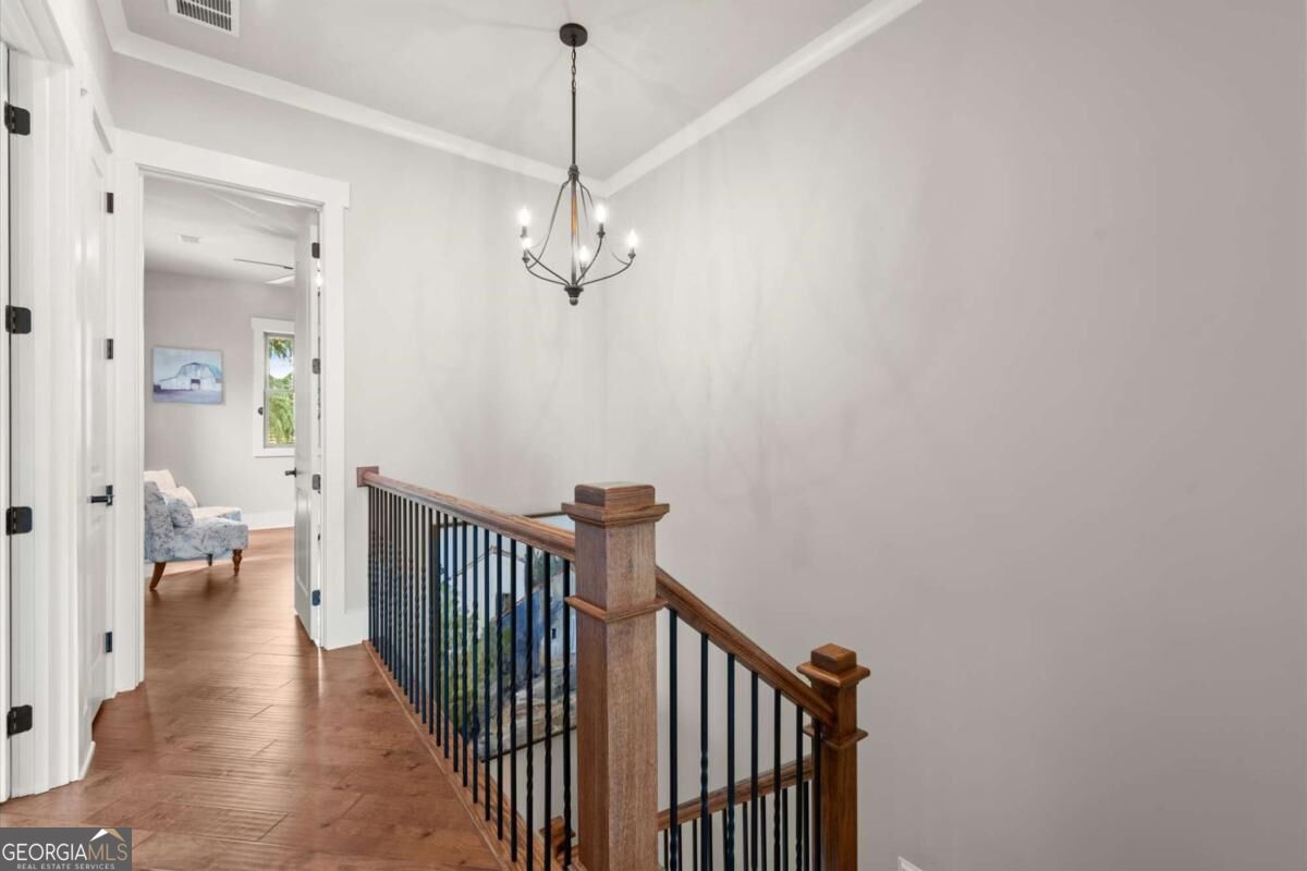 Upstairs landing with wood flooring, a wood-and-metal stair railing, and a chandelier.