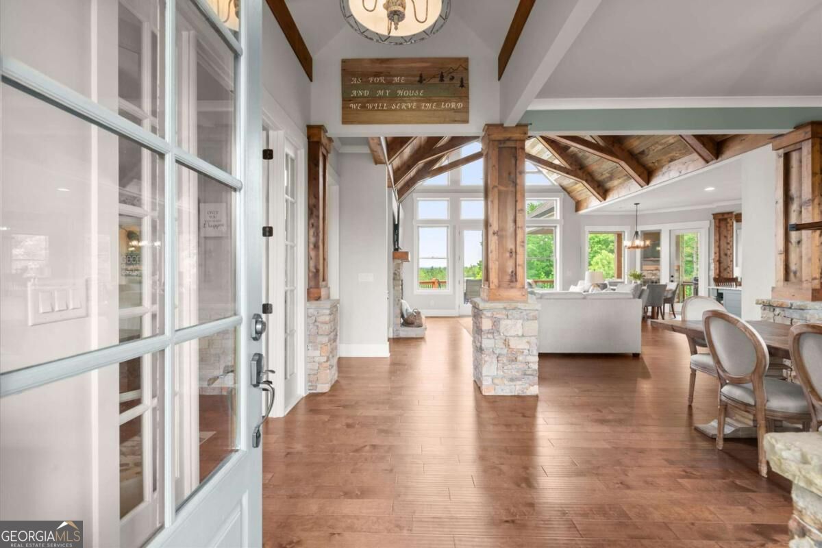 Open living and dining area with exposed timber beams, stone columns, and wide-plank wood floors.
