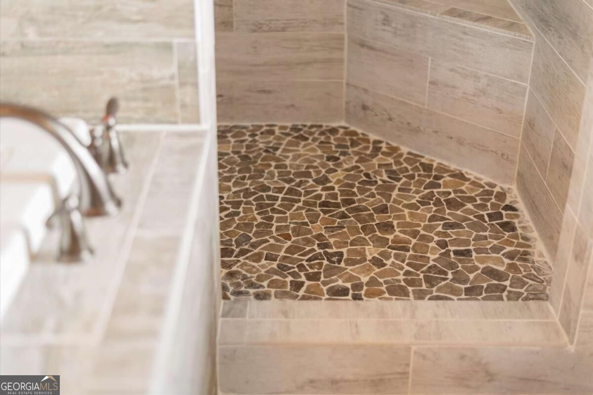 Walk-in shower with a pebble-mosaic floor and beige stone tile walls.