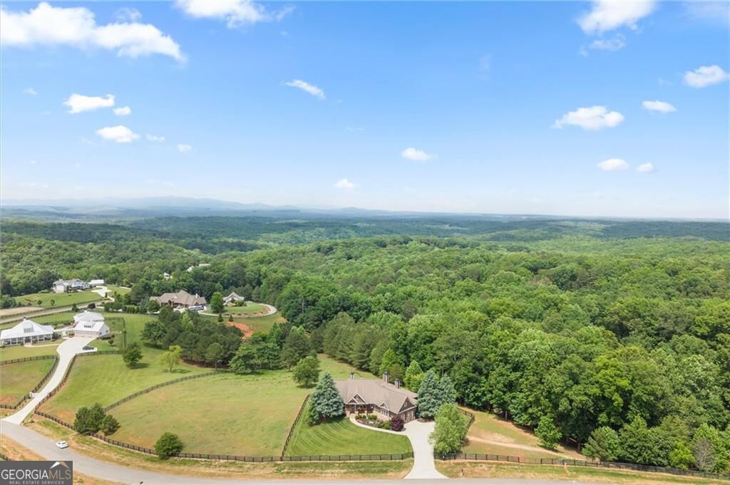 Aerial view of a home beside wooded hills, lawns, and neighboring properties.