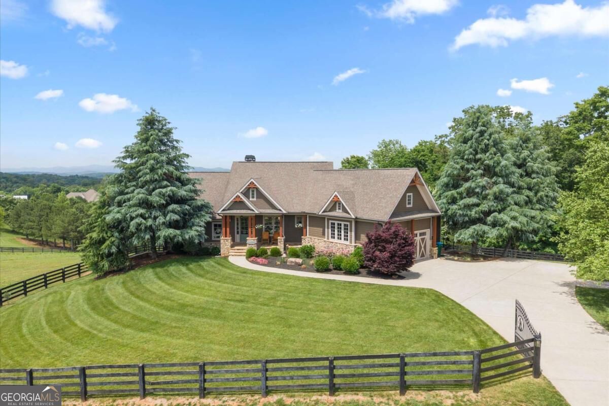 Aerial view of a single-story home with a fenced lawn and broad driveway.