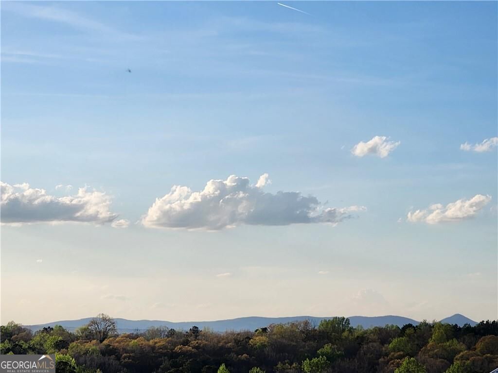 Wooded hills and distant blue mountains beneath a bright sky with scattered clouds.