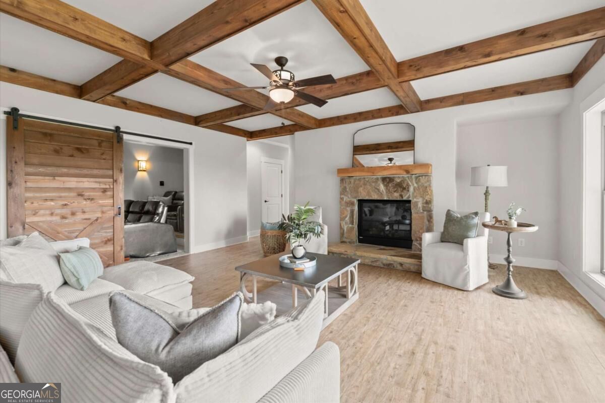 Living room with exposed wood beams, a stone fireplace, and a sliding barn door.