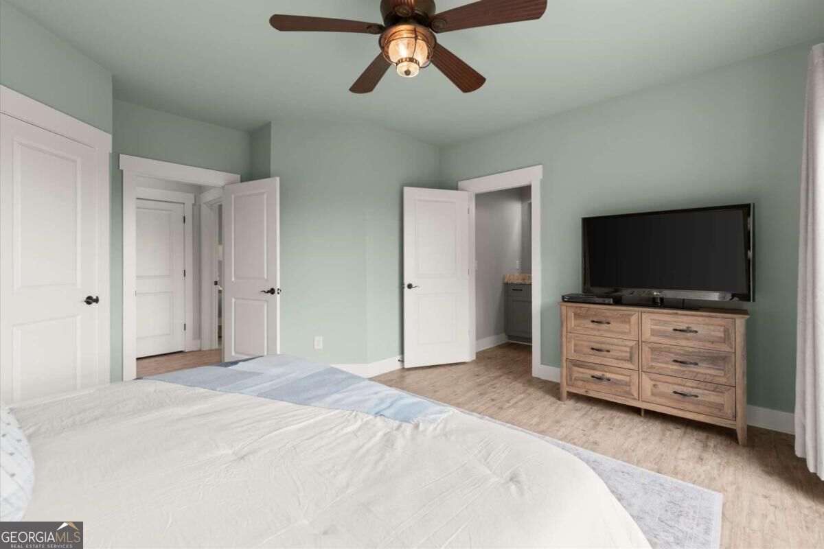Bedroom with a large bed, pale green walls, ceiling fan, and television on a dresser.