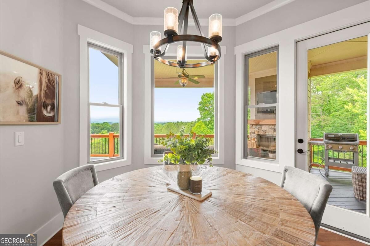 Dining room with a round wood table, chandelier, and windows overlooking a wooded deck.