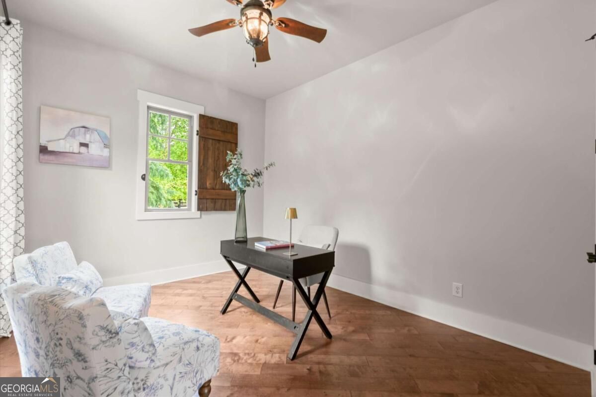 Staged home office with an X-leg desk, floral armchair, and window with a wooden shutter.