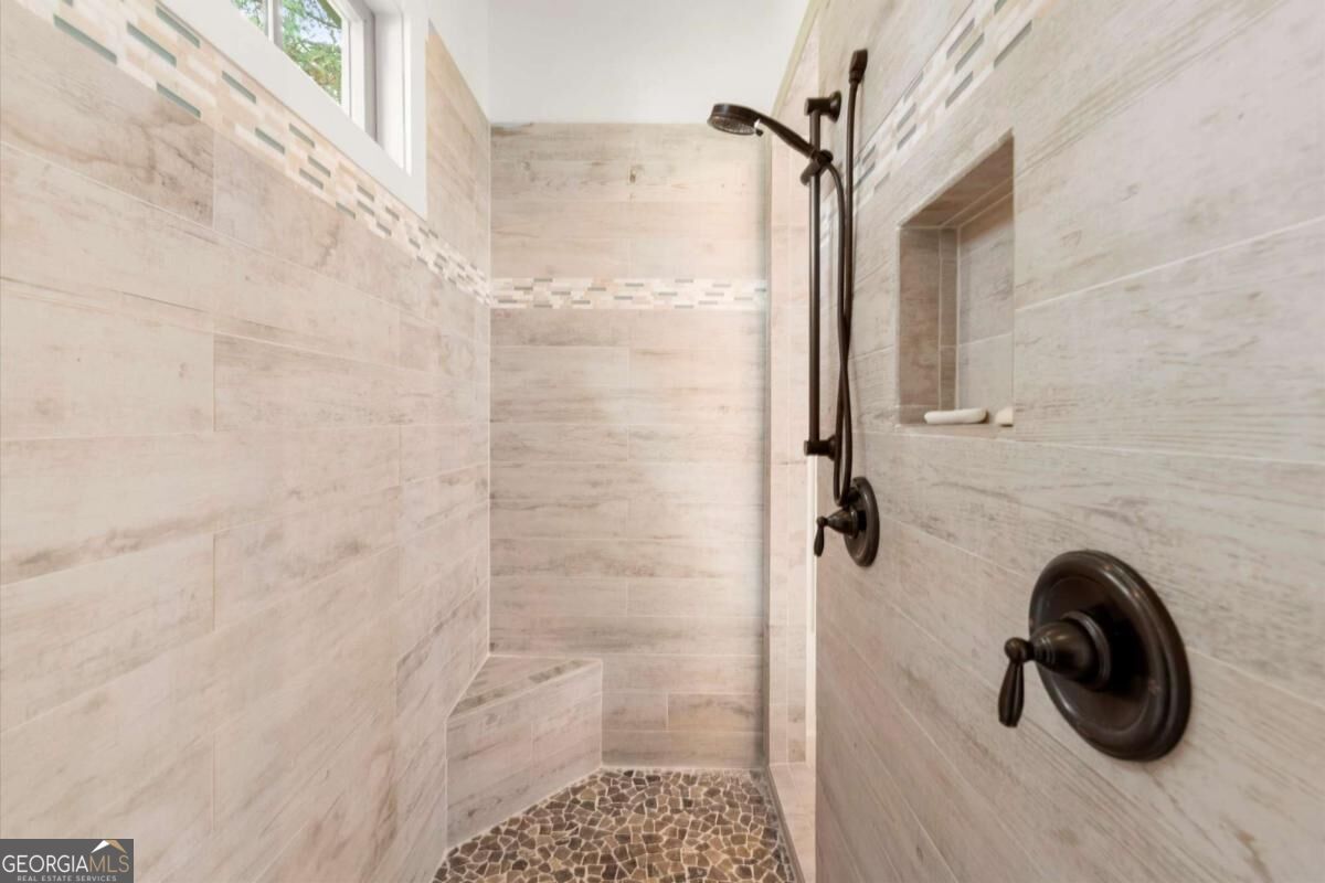 Walk-in shower with pale tile, pebble mosaic floor, built-in bench, and dark bronze fixtures.
