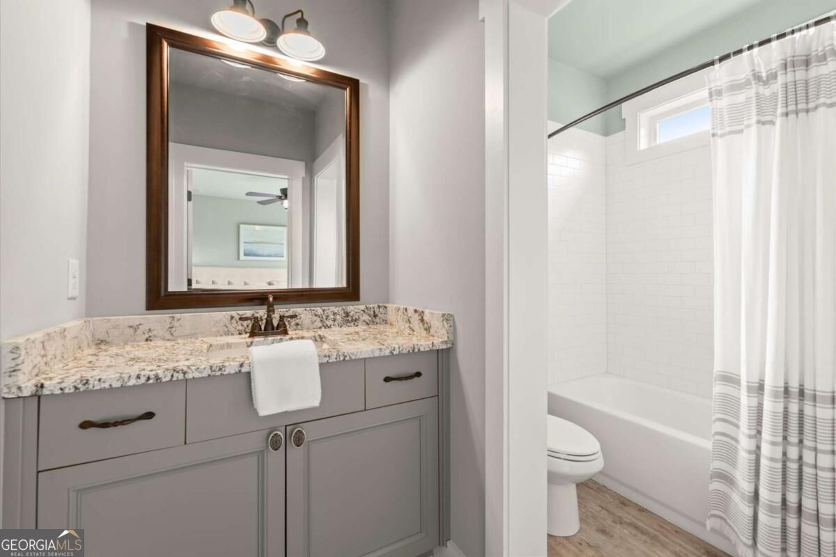 Bathroom with a gray vanity and stone countertop beside a white-tiled tub and shower.