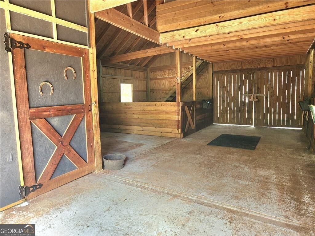 Wooden horse stable with a stall, open plank doors, and exposed rafters.