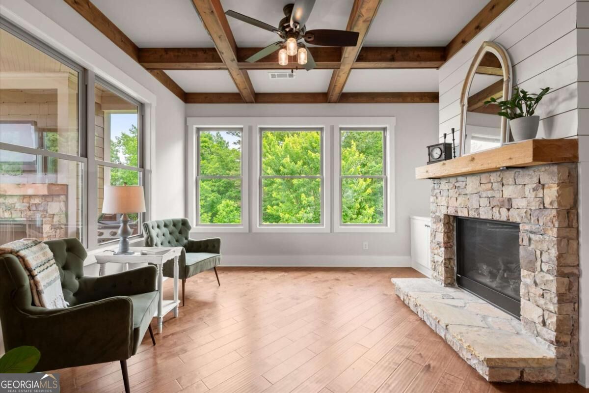 Living room with exposed wood ceiling beams, stone fireplace, and three large windows.