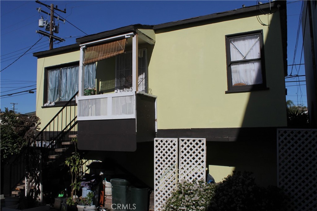Raised pale-yellow house with a small balcony, exterior stairs, and white lattice panels.