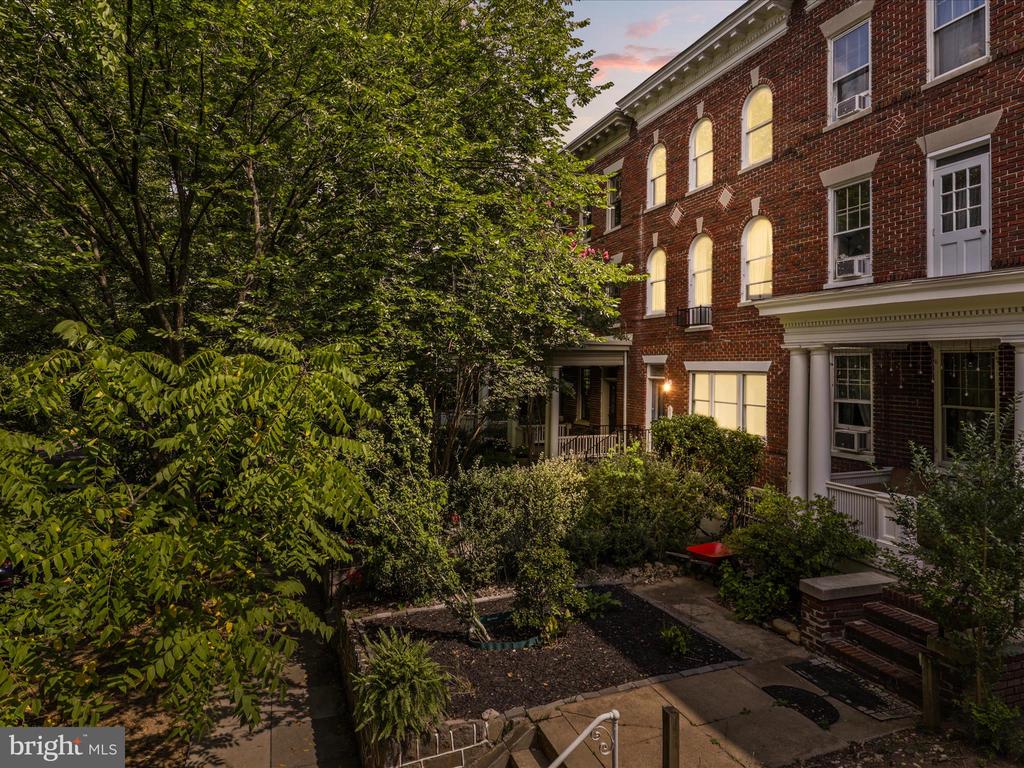 Red-brick townhouses overlooking a leafy courtyard with garden beds and stone paths at dusk.