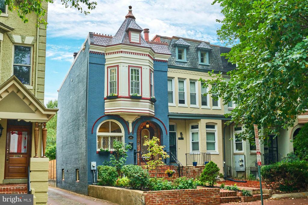 Blue Victorian rowhouse with a turret bay, arched windows, and a landscaped brick-front garden.