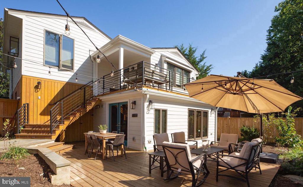 White two-story home with a balcony and furnished deck under a large tan umbrella.