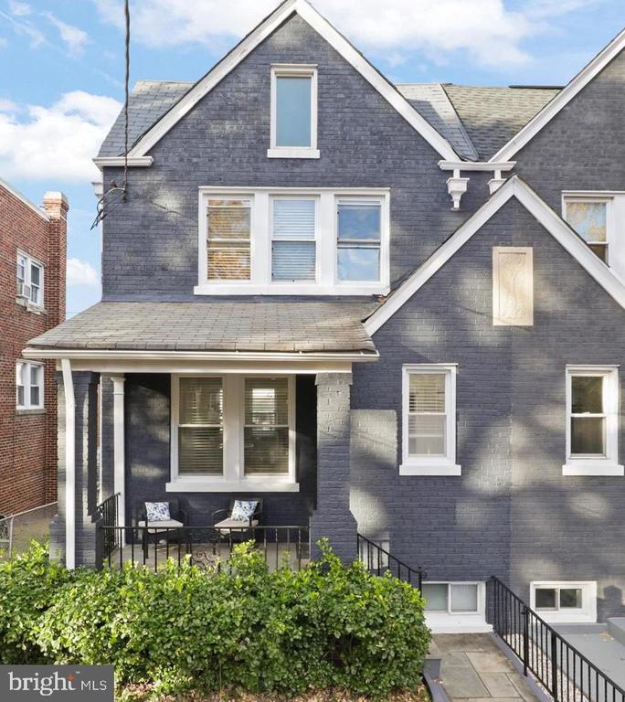 Dark gray home with white-trimmed gables, a covered porch, and a leafy hedge.