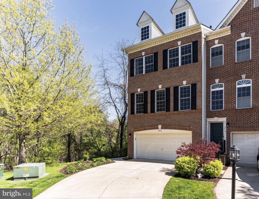 Red-brick townhouse with black shutters, a front-entry garage, and a curved driveway.