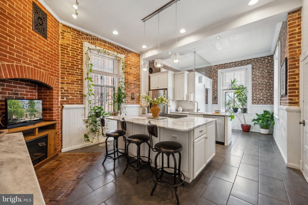 Kitchen with a marble island, bar stools, exposed brick walls, and a brick fireplace.