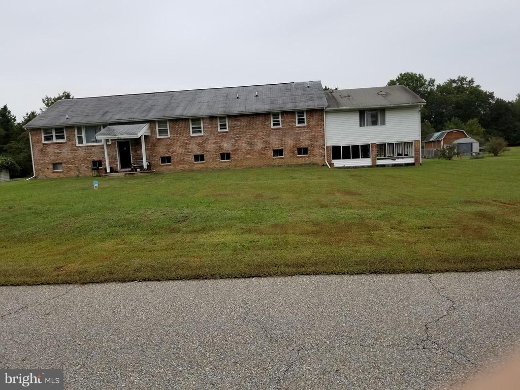 Long brick house with a white-sided section, broad lawn, and small outbuilding.