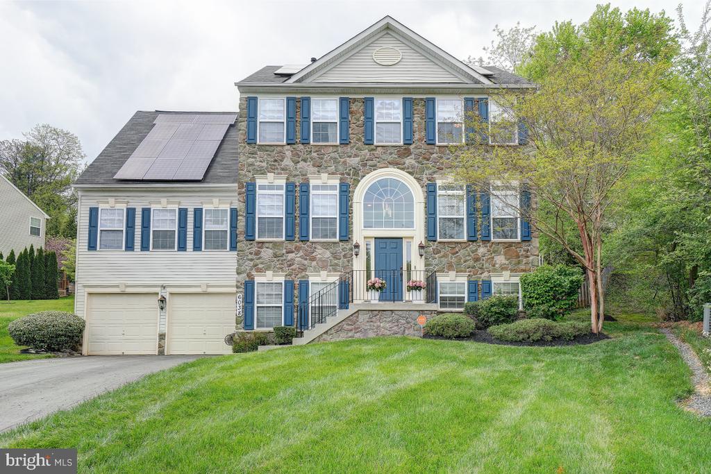 Two-story stone-front house with blue shutters, solar panels, and an arched entry.