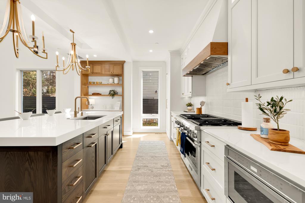 Bright modern kitchen with a dark wood island, white cabinetry, and brass chandeliers.