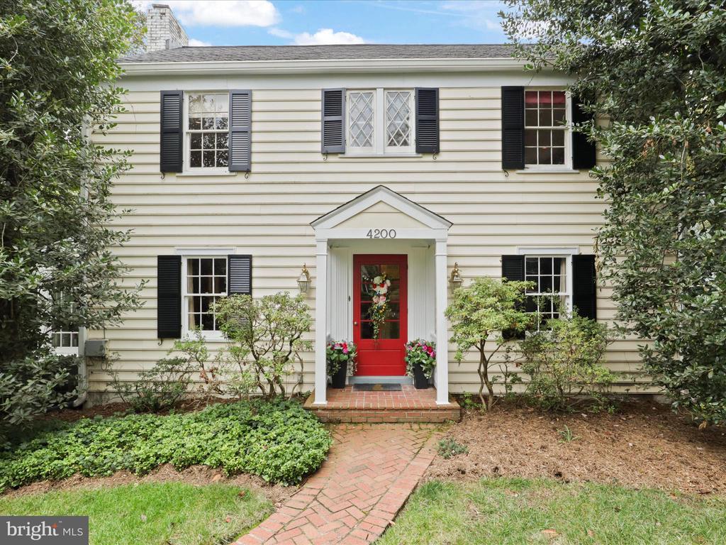 White two-story house with black shutters, a red front door, and a brick walkway.