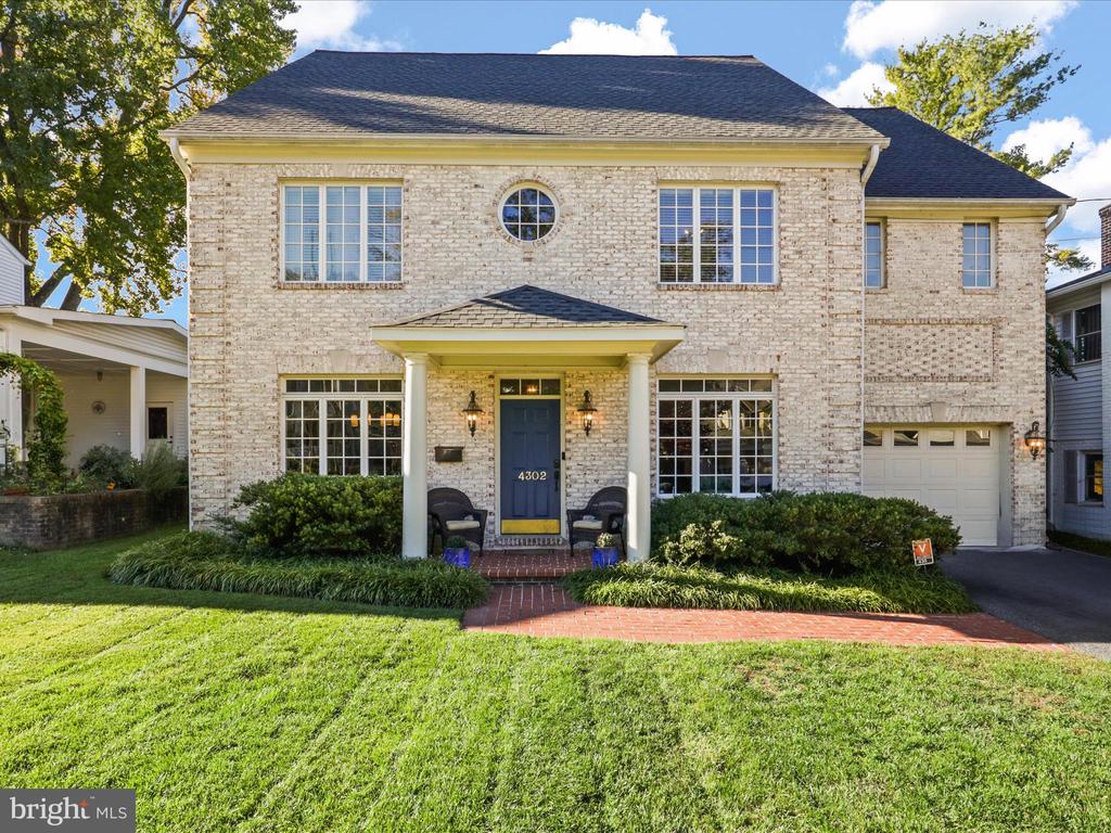 Two-story brick house with a blue front door, attached garage, and landscaped front lawn.