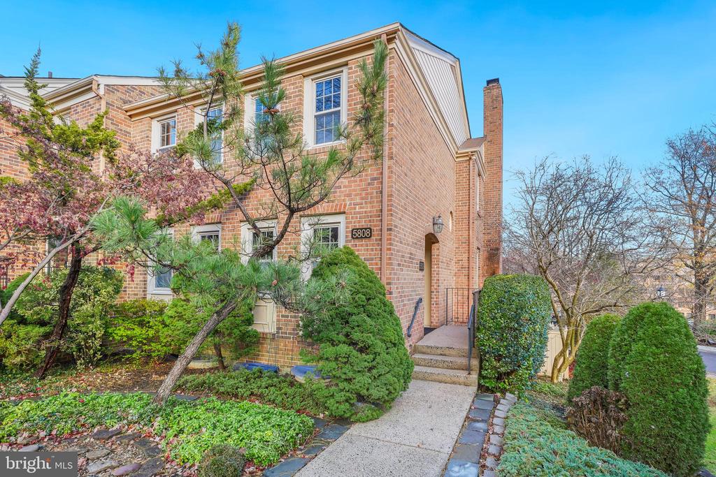 Two-story brick townhouse with a front walkway, steps, and mature landscaping.