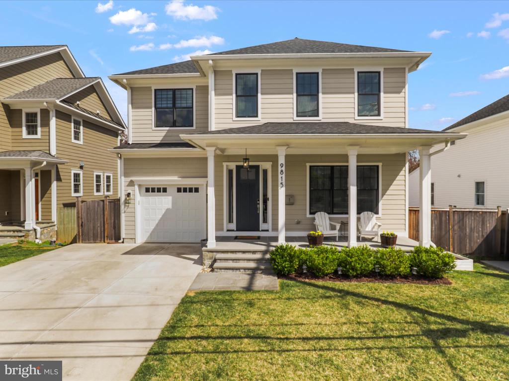 Two-story beige house with an attached garage, covered porch, and landscaped front yard.