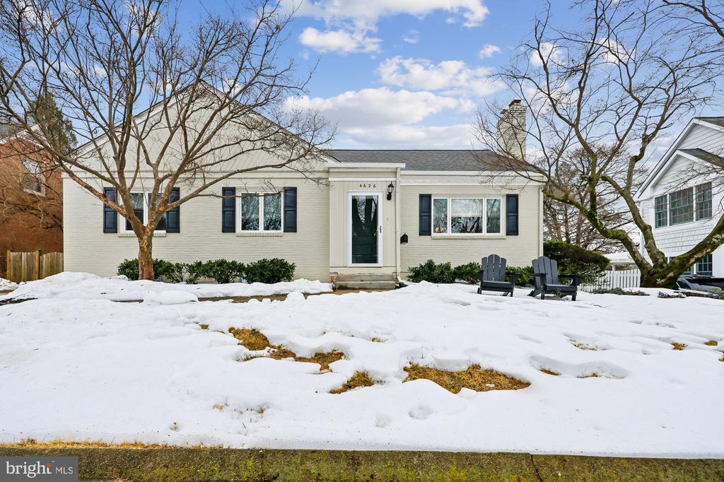White brick single-story home with dark shutters, front door, and snow-covered lawn.