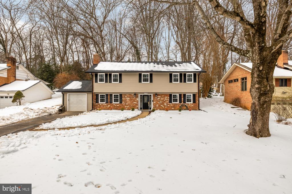 Split-level brick and beige home with an attached garage, photographed in a snow-covered yard.