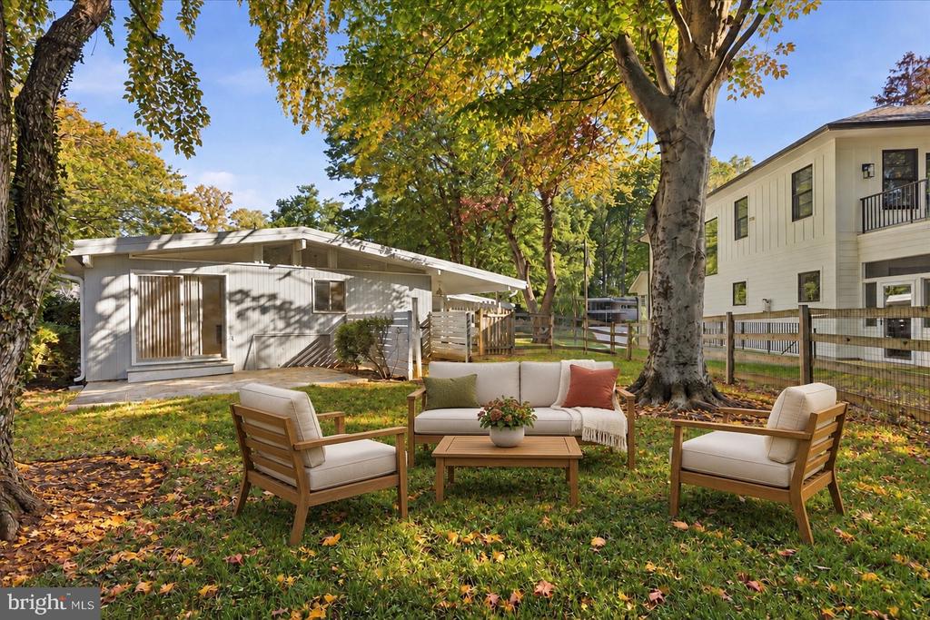 Backyard seating beneath mature autumn trees, with a single-story home and neighboring house beyond.