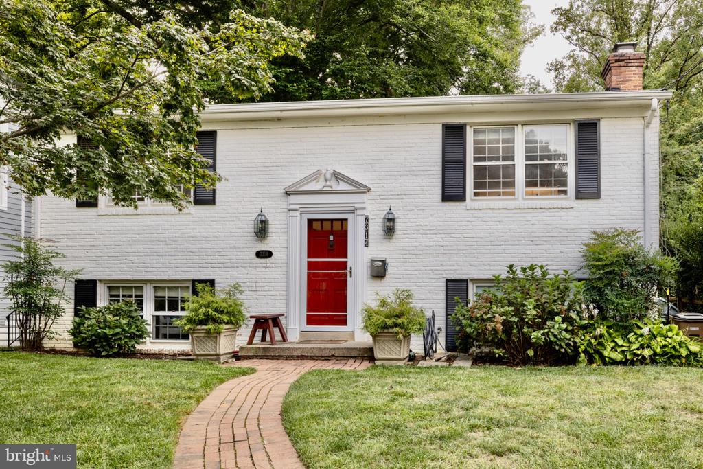 White brick house with black shutters, a red front door, and a curved brick walkway.