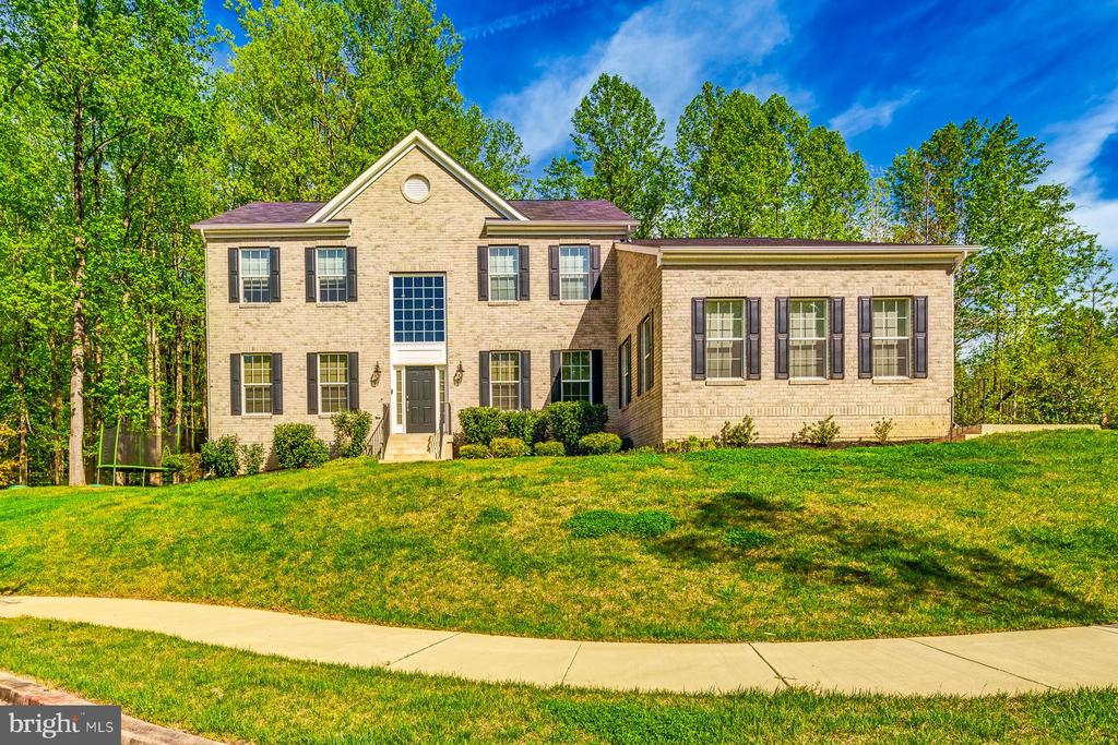 Two-story brick house with a gabled entrance, dark shutters, and a broad green lawn.
