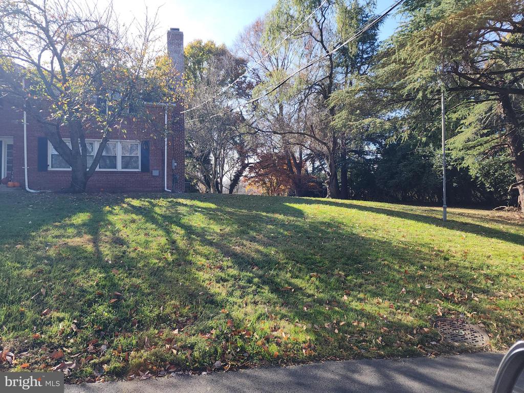 Red-brick house beside a sloping lawn beneath mature trees.