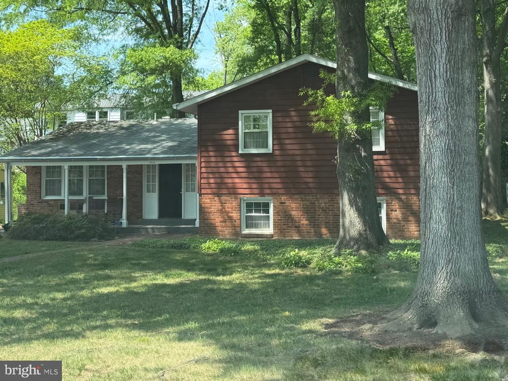 Two-story brick and red-brown home with a covered entry and mature trees across the lawn.