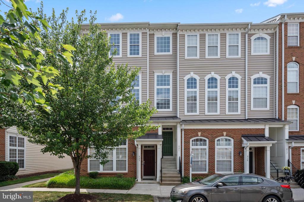 Attached townhouses with beige siding and brick lower floors, partly screened by a leafy tree.