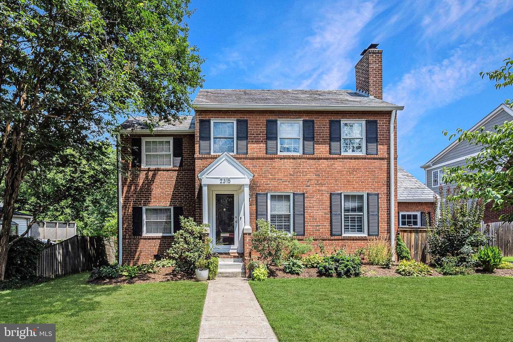 Two-story red brick house with black shutters, a white-trimmed entrance, and a front walkway.