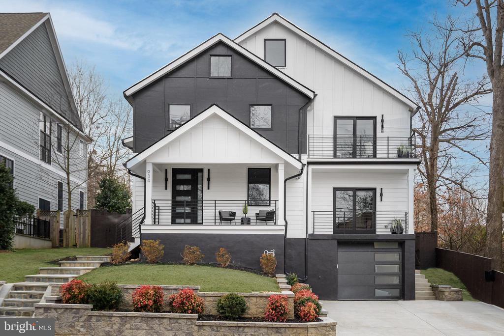Modern white-and-charcoal home with balconies, a covered porch, attached garage, and landscaped sloped yard.