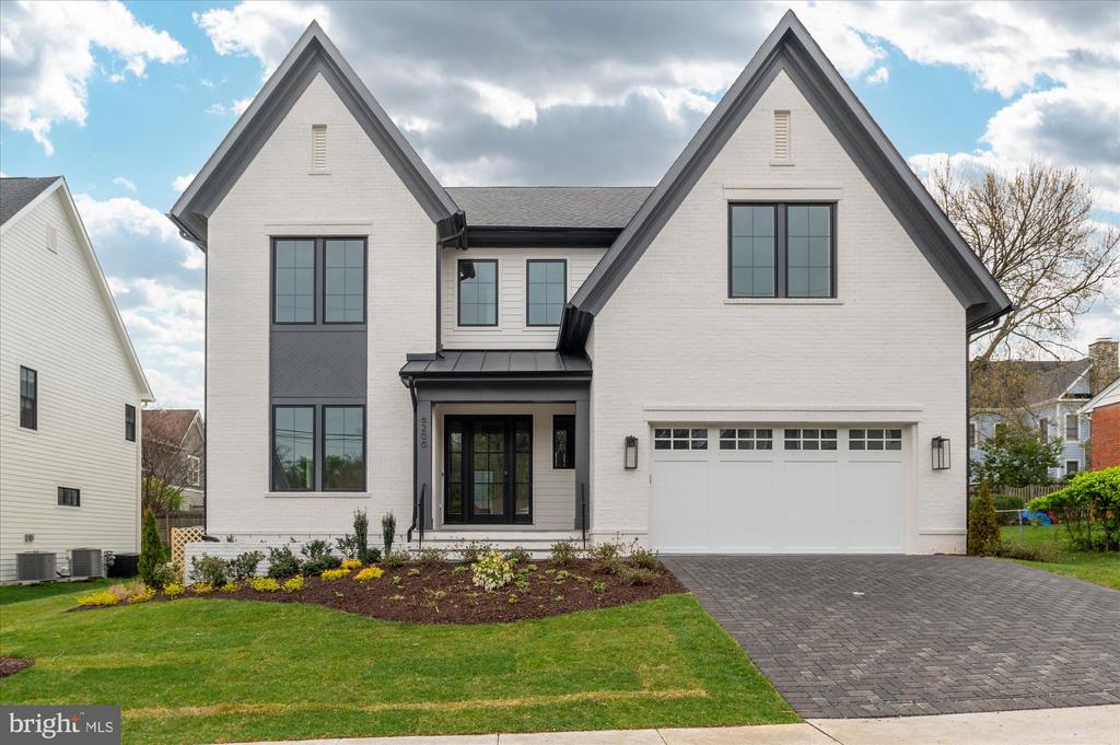 White-brick house with two steep gables, dark trim, landscaped front beds, and a paved driveway.