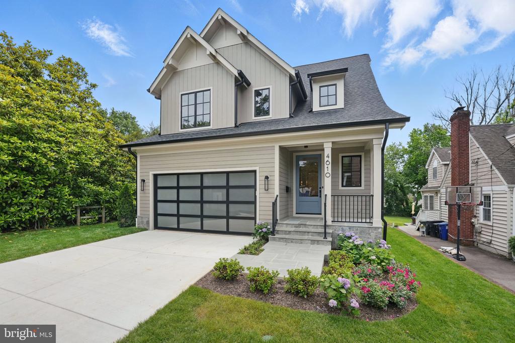 Two-story light-colored house with a black-framed garage door, covered entry, and landscaped front garden.
