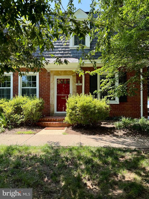 Two-story brick home with a red front door, white trim, and mature trees.