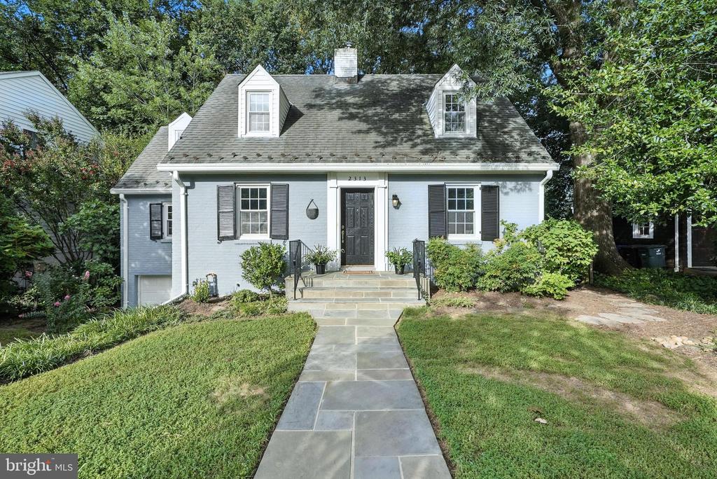 Light blue-gray Cape Cod house with dark shutters, two dormers, and a stone front walkway.