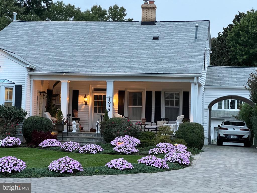 White house with a columned porch, arched garage passage, and pink flower beds.