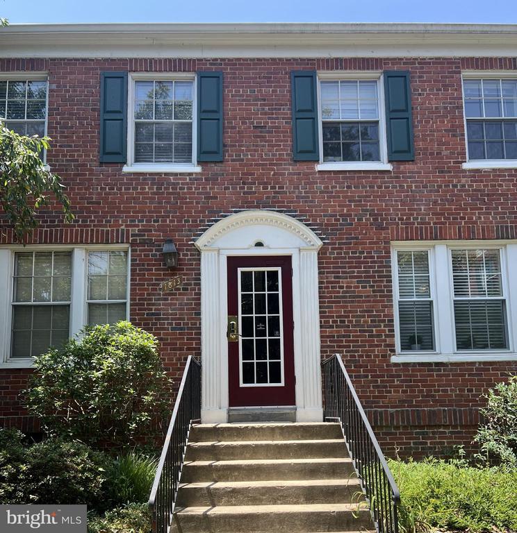 Red-brick home entrance with dark shutters, burgundy door, and steps with black railings.