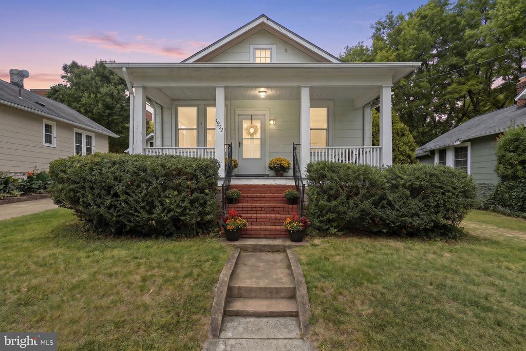 Bungalow with a covered porch, white railings, and brick steps at dusk.