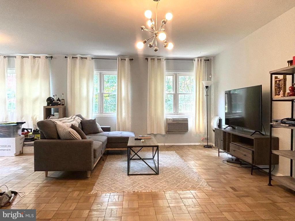 Living room with a gray sectional, patterned rug, parquet flooring, and tall curtained windows.